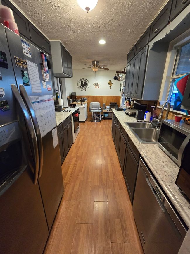 Kitchen featuring a wainscoted wall, stainless steel appliances, light countertops, light wood-style floors, and a textured ceiling | Image 19