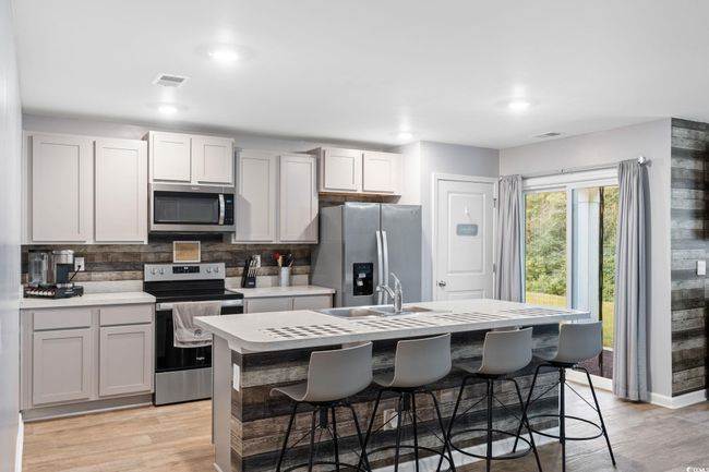 Kitchen with a kitchen breakfast bar, a kitchen island with sink, stainless steel appliances, and light hardwood / wood-style floors | Image 4