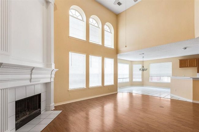 Unfurnished living room with a high ceiling, visible vents, light wood-style floors, a tiled fireplace, and a notable chandelier | Image 6