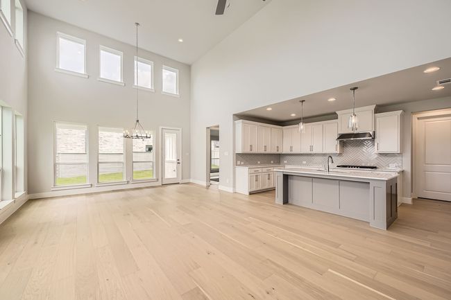Kitchen featuring a towering ceiling, light countertops, backsplash, light wood-style floors, and white cabinetry | Image 6