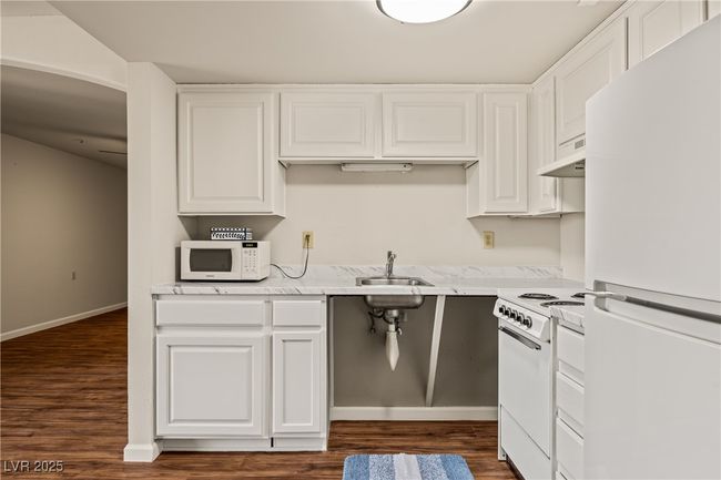 Kitchen with a sink, white cabinetry, under cabinet range hood, and white appliances | Image 4
