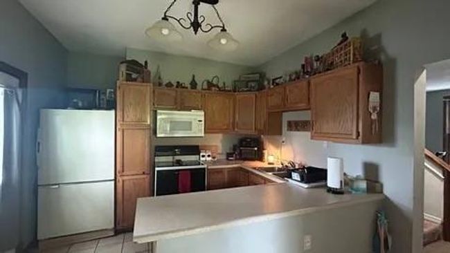 Kitchen with a chandelier, light tile patterned floors, kitchen peninsula, stainless steel fridge, and stove | Image 10