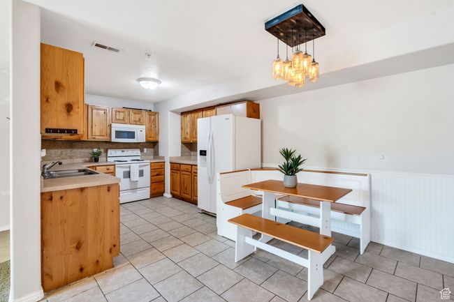 Kitchen featuring white appliances, light countertops, light tile patterned flooring, decorative backsplash, and a chandelier | Image 6