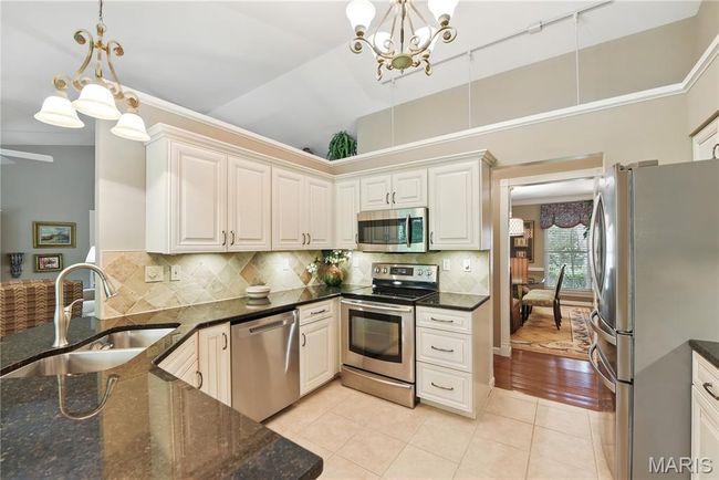 Kitchen featuring stainless steel appliances, a chandelier, light tile patterned floors, hanging light fixtures, and tasteful backsplash | Image 8