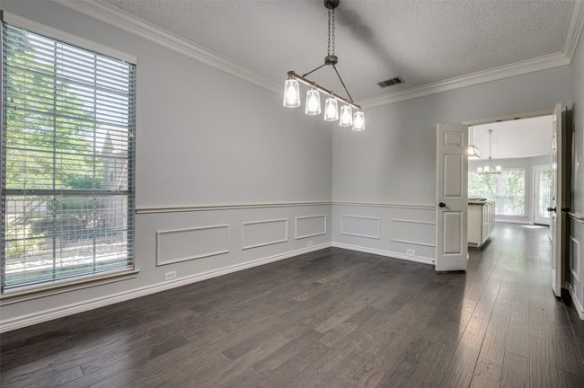 Empty room featuring a wainscoted wall, dark wood-type flooring, crown molding, a textured ceiling, and a notable chandelier | Image 9