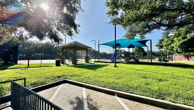 This photo shows a well-maintained community park featuring a shaded playground, a picnic pavilion, and a tennis court, surrounded by lush greenery and mature trees, perfect for family recreation. | Image 18