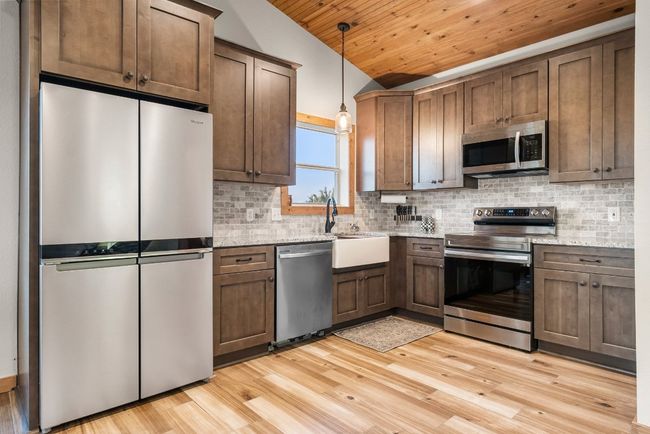 Kitchen with tasteful backsplash, lofted ceiling, light wood-style flooring, appliances with stainless steel finishes, and a sink | Image 18