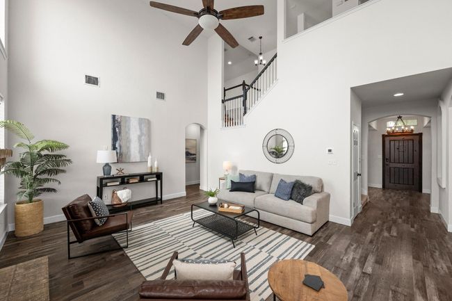 Living area featuring arched walkways, a high ceiling, dark wood-style flooring, a chandelier, and a ceiling fan | Image 4