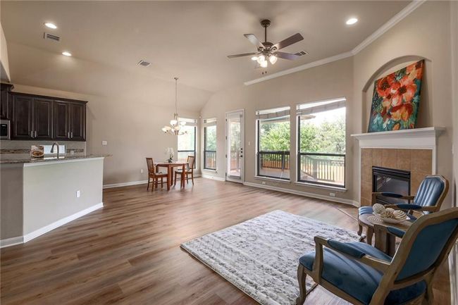 Living area featuring a chandelier, a ceiling fan, wood finished floors, crown molding, and a fireplace | Image 5