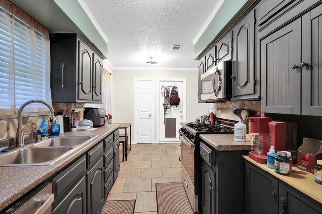 Kitchen featuring stainless steel appliances, tasteful backsplash, a textured ceiling, ornamental molding, and light stone finish flooring | Image 12