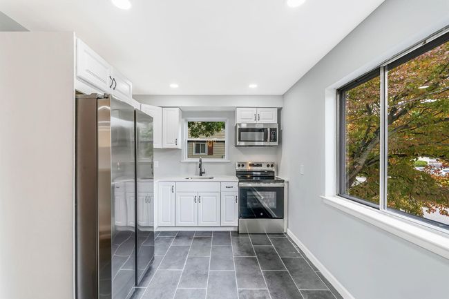 Kitchen featuring light countertops, baseboards, appliances with stainless steel finishes, white cabinetry, and a sink | Image 8