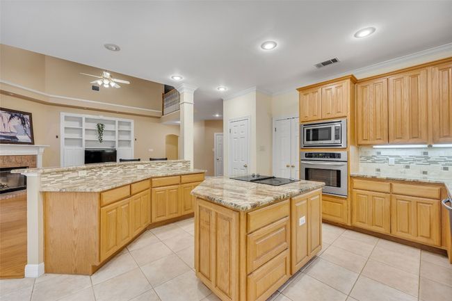Kitchen with stainless steel appliances, a kitchen island, crown molding, a ceiling fan, and backsplash | Image 17