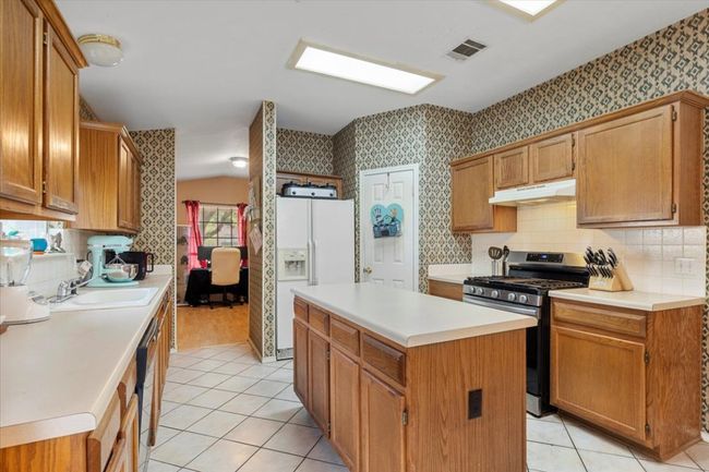 Kitchen with stainless steel gas range, under cabinet range hood, white refrigerator with ice dispenser, a sink, and wallpapered walls | Image 9
