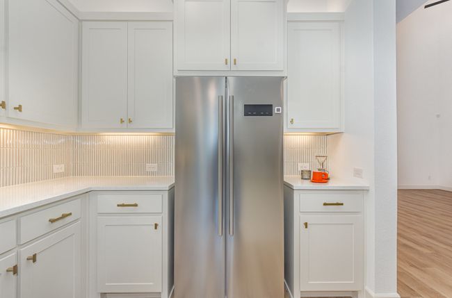 Kitchen with high end refrigerator, light countertops, light wood-style floors, and white cabinets | Image 8
