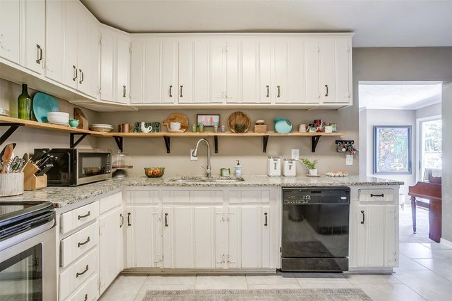 Kitchen with appliances with stainless steel finishes, open shelves, light tile patterned floors, white cabinets, and light stone counters | Image 10