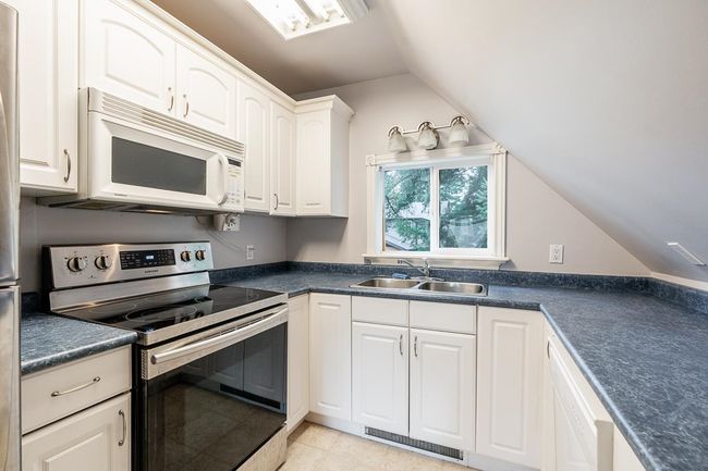 Kitchen with white appliances, dark countertops, visible vents, and a sink | Image 30