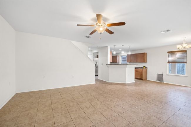 Unfurnished living room with ceiling fan with notable chandelier, visible vents, baseboards, and light tile patterned floors | Image 38