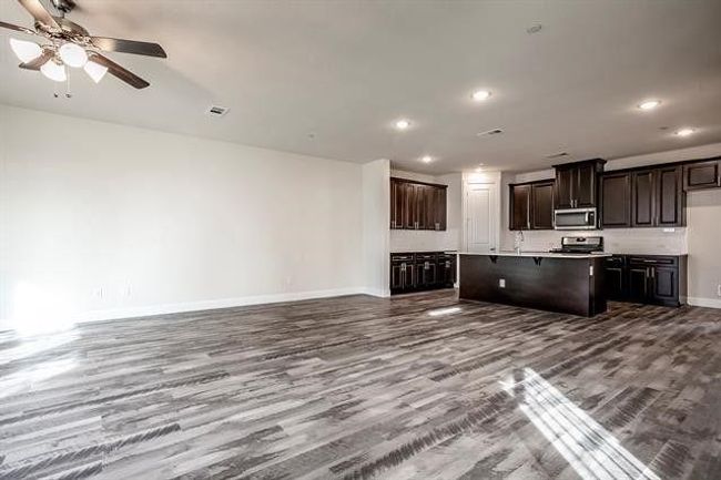 Kitchen featuring baseboards, open floor plan, dark wood-type flooring, a kitchen island with sink, and stainless steel appliances | Image 6