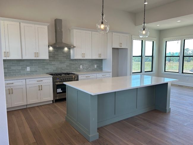 Kitchen featuring high end stainless steel range, wall chimney range hood, wood finished floors, white cabinetry, and recessed lighting | Image 4