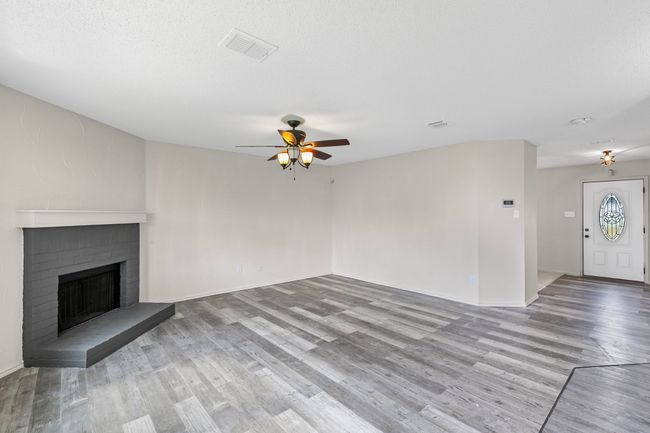 Unfurnished living room with ceiling fan, wood finished floors, and a brick fireplace | Image 5