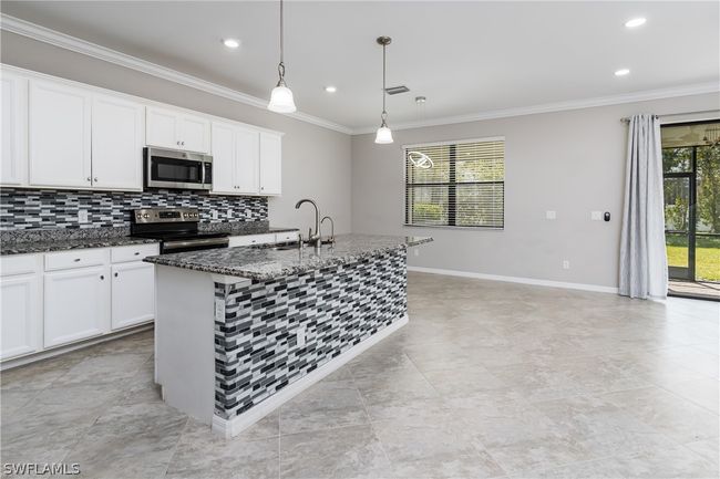 Kitchen featuring stainless steel appliances, a center island with sink, dark stone countertops, white cabinets, and pendant lighting | Image 7