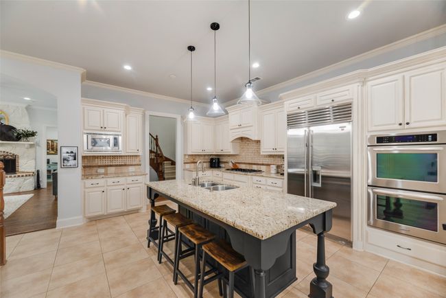 Kitchen with built in appliances, a kitchen bar, decorative backsplash, light stone counters, and ornamental molding | Image 4