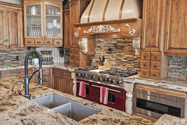 Kitchen featuring brown cabinetry, light stone countertops, backsplash, range with two ovens, and built in microwave | Image 23