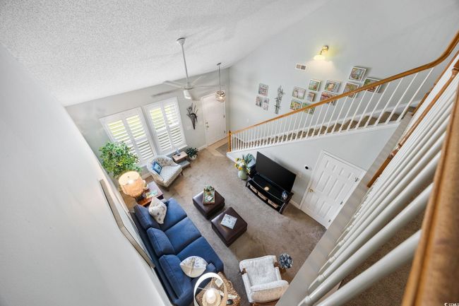 Carpeted living area with a textured ceiling, stairs, high vaulted ceiling, and ceiling fan | Image 29