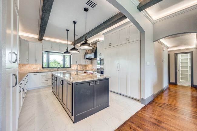 Kitchen featuring arched walkways, light stone counters, decorative backsplash, an island with sink, and crown molding | Image 5