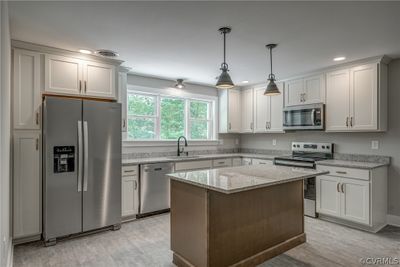 Kitchen with hanging light fixtures, a kitchen island, appliances with stainless steel finishes, white cabinets, and sink | Image 1