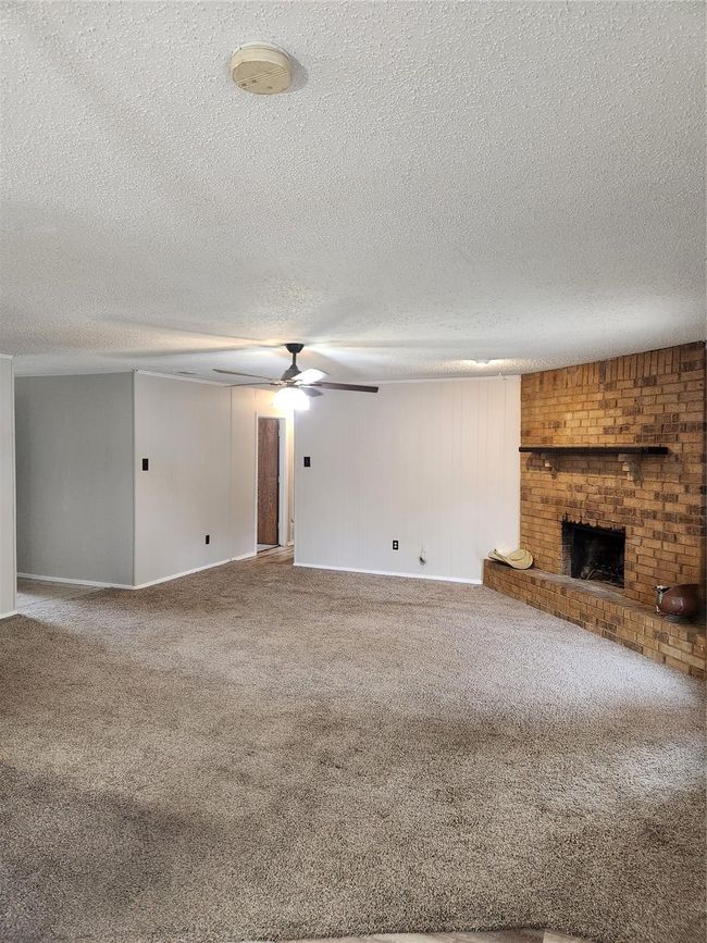 Unfurnished living room featuring carpet floors, a ceiling fan, a fireplace, a textured ceiling, and baseboards | Image 4