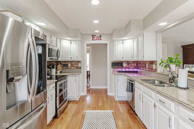 kitchen with recessed lighting, stainless steel appliances, a sink, light stone countertops, and white cabinetry | Image 11