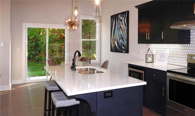 Kitchen with stainless steel electric range oven, light countertops, a kitchen island with sink, a sink, and under cabinet range hood | Image 21