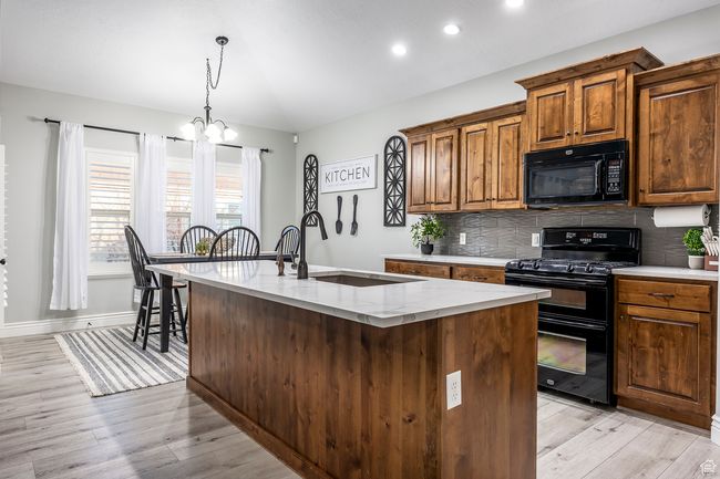 Kitchen featuring sink, a kitchen island with sink, light stone counters, tasteful backsplash, and black appliances | Image 5