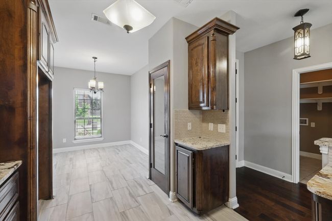 Kitchen featuring a chandelier, decorative backsplash, light stone counters, and dark brown cabinets | Image 7