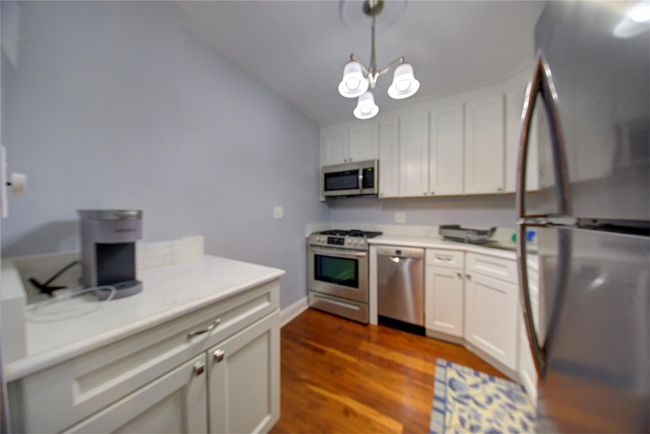 Kitchen featuring dark wood finished floors, stainless steel appliances, light countertops, hanging light fixtures, and white cabinets | Image 5