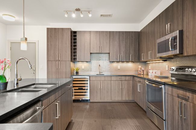 Kitchen with appliances with stainless steel finishes, wine cooler, a sink, dark stone countertops, and dark wood-style flooring | Image 28