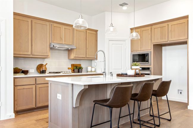 Kitchen featuring appliances with stainless steel finishes, under cabinet range hood, tasteful backsplash, a center island with sink, and light countertops | Image 16