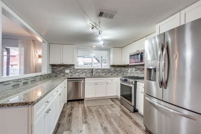 Kitchen featuring light stone countertops, white cabinets, appliances with stainless steel finishes, track lighting, and sink | Image 12