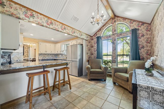 Kitchen with wallpapered walls, an inviting chandelier, a peninsula, freestanding refrigerator, and vaulted ceiling with beams | Image 13