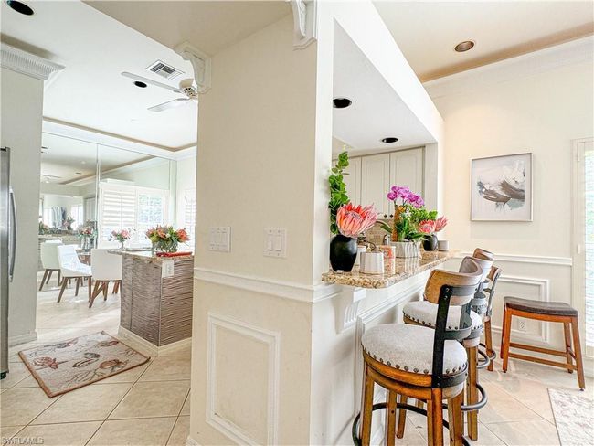 Kitchen featuring light tile floors, light stone counters, ceiling fan, and a breakfast bar | Image 35