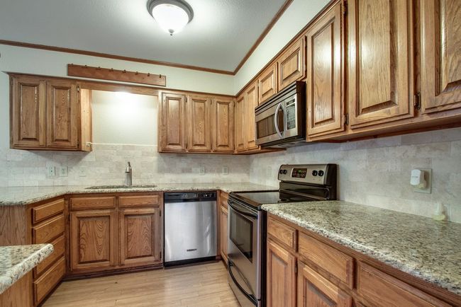 Kitchen with appliances with stainless steel finishes, brown cabinetry, ornamental molding, decorative backsplash, and light wood-style floors | Image 11