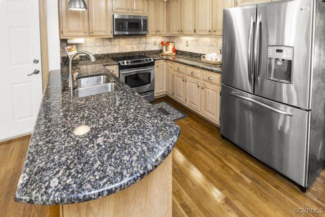 Kitchen with stainless steel appliances, a sink, dark wood-style flooring, dark stone counters, and tasteful backsplash | Image 11