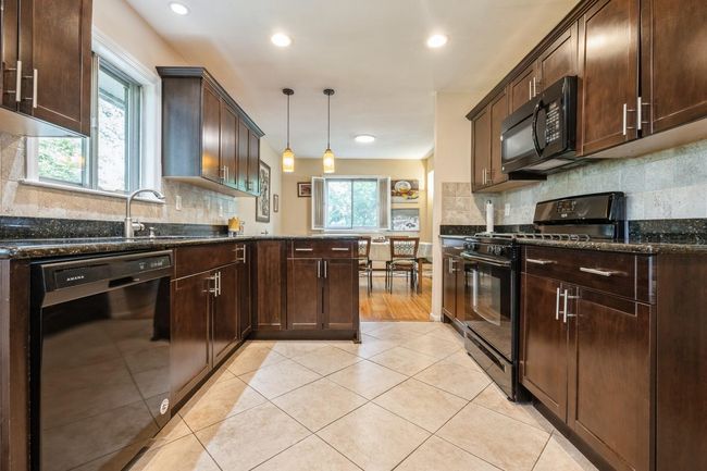 Kitchen with black appliances, dark stone counters, dark brown cabinets, decorative backsplash, and hanging light fixtures | Image 10