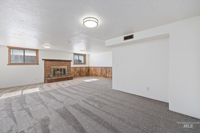 Unfurnished living room featuring a textured ceiling, carpet, wood walls, wainscoting, and a fireplace | Image 26