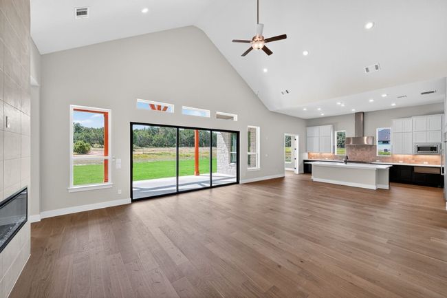 Unfurnished living room featuring high vaulted ceiling, a tiled fireplace, light wood-type flooring, recessed lighting, and a ceiling fan | Image 4