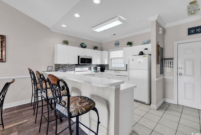 Kitchen with freestanding refrigerator, a peninsula, stainless steel microwave, stove, and a breakfast bar area | Image 5