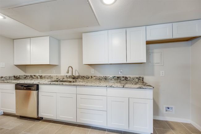 Kitchen with dishwasher, white cabinets, light stone countertops, and sink | Image 12
