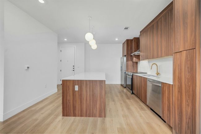 Kitchen with stainless steel appliances, modern cabinets, a kitchen island, light countertops, and brown cabinetry | Image 4