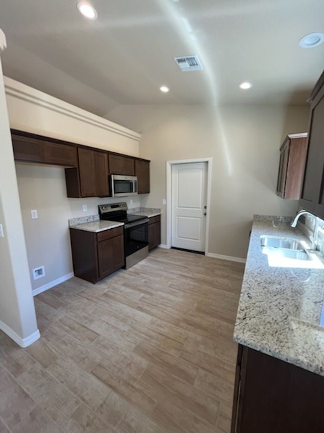 Kitchen with stainless steel appliances, a sink, baseboards, dark brown cabinets, and vaulted ceiling | Image 13